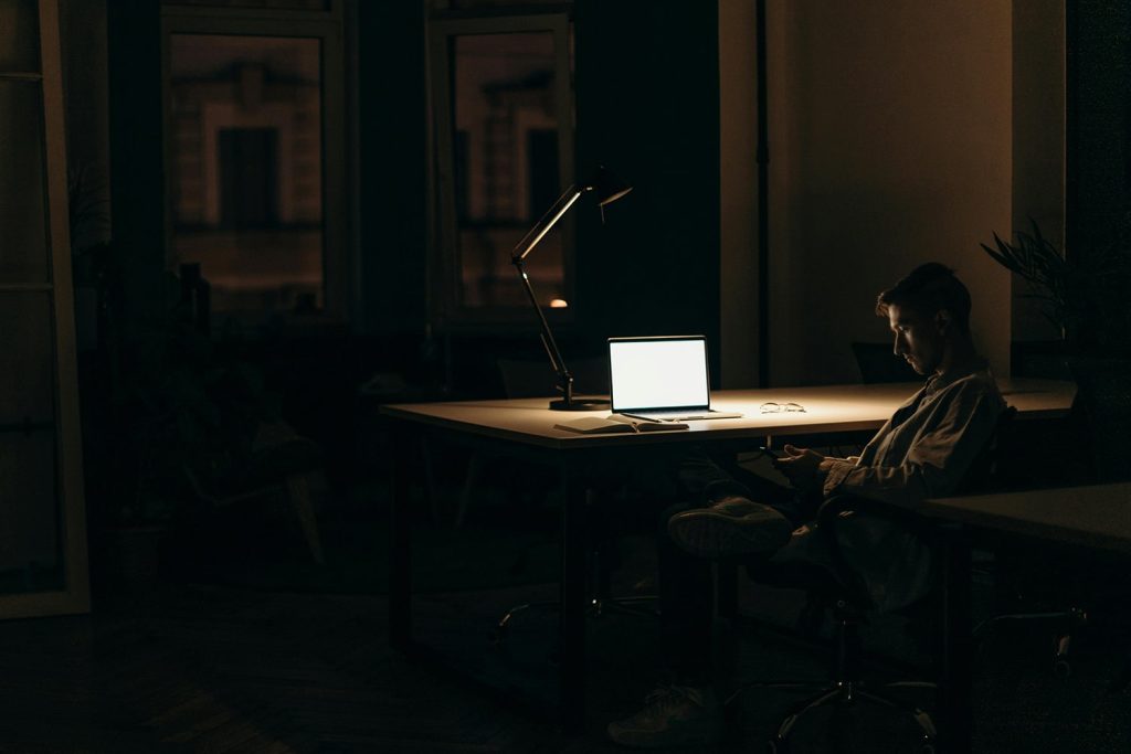 Man sitting alone in a dark room, near his laptop