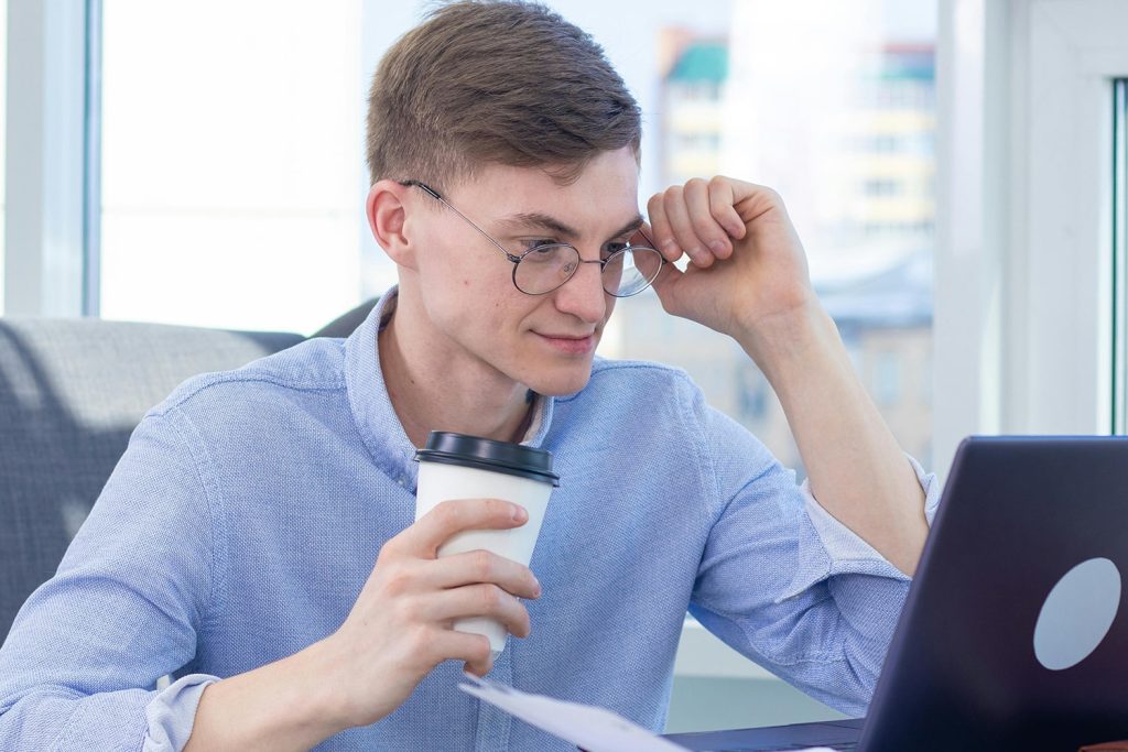 Man looking at his laptop, holding a cup of coffee