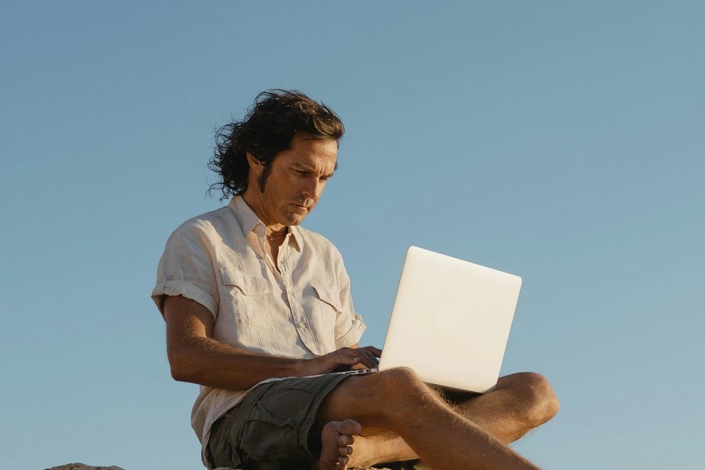 A man sitting on a rock, working on his laptop
