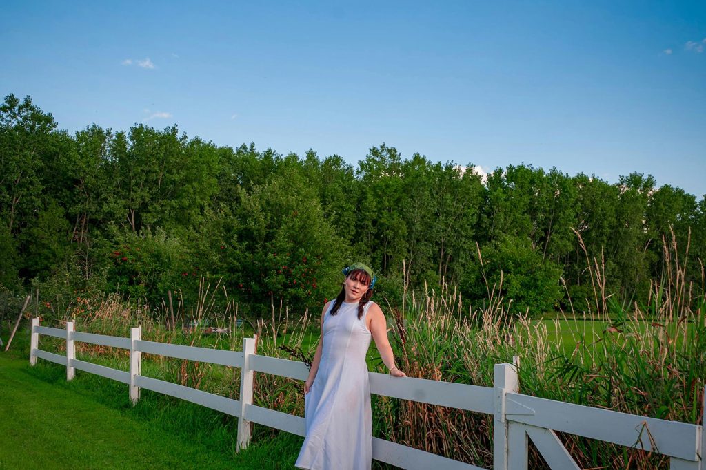 Woman stands near fence in an open field in a small town