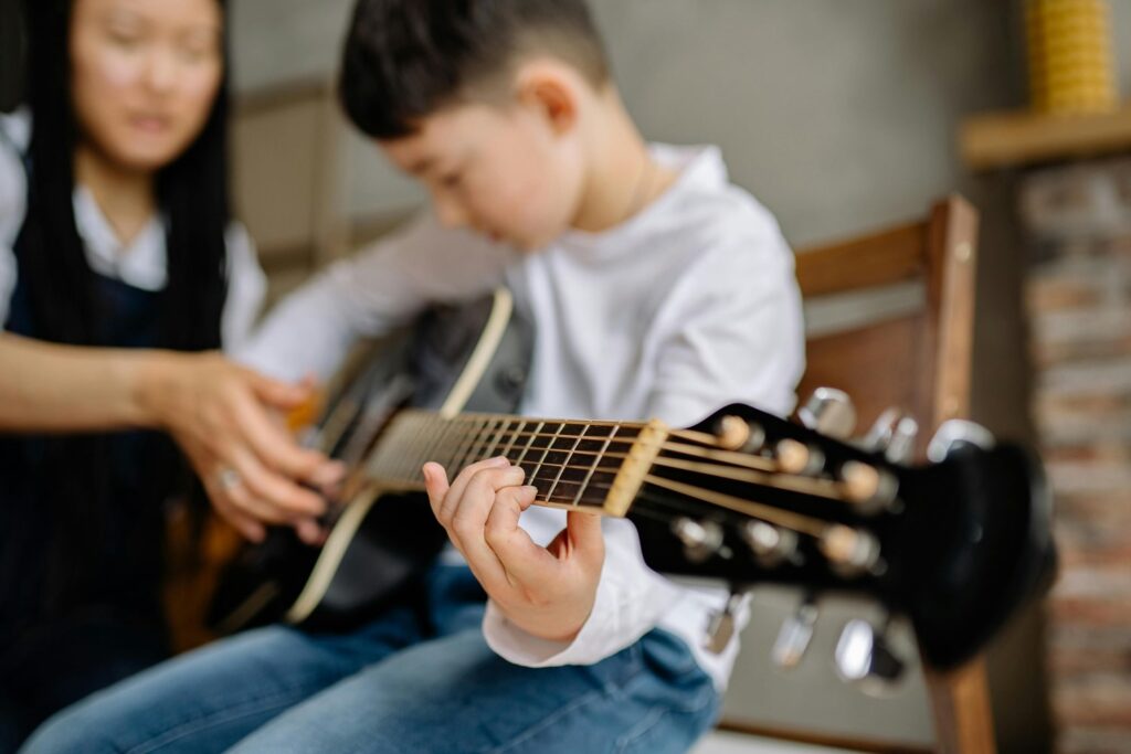 A woman teaching a young boy how to play guitar